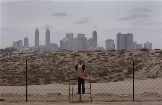 With a view of towers along the Sheikh Zayed highway in background, an Asian laborer fixes new fence around a horse race track which was divided to two parts by a new road construction at Al Barsha district Sunday, Nov. 27, 2011 in Dubai, United Arab Emirates. 